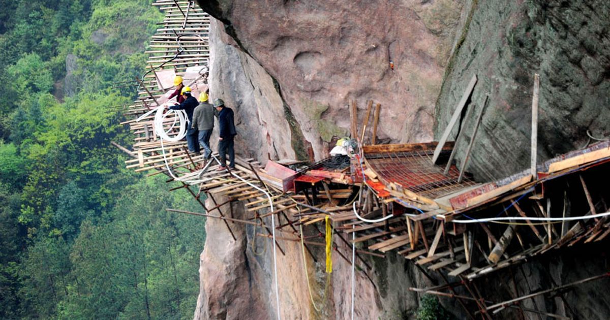 Workers stretch a long hose to pave a road on the cliff of a mountain